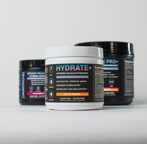 Three supplement tubs from iAMINOS on a clean white studio background: a front white tub labeled HYDRATE+ Solar Orange, with two darker black-and-pink tubs behind it labeled iAMINOS Athlete Pro+ and iAMINOS Brain Health+.