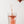 A hand holding a clear scoop of iAMINOS Hydrate+. pouring a fine pink powder into a clear glass of water, creating a bubbly orange liquid, on a clean white background.